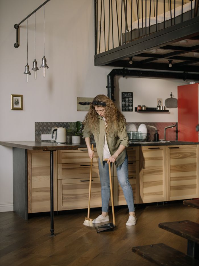 A woman with curly hair sweeps a modern loft kitchen, creating a cozy home atmosphere.