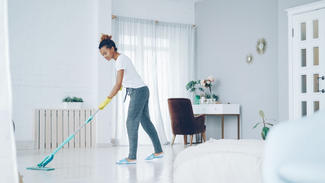 hero-img Pretty African American girl is mopping floor at home with flat plastic mop wearing gloves and wear-at-home clothing. Modern interiors, cleanness and young people concept.