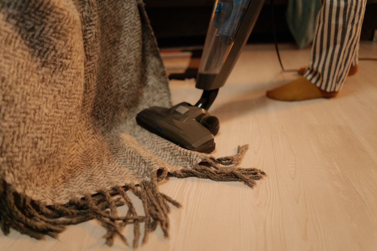 services-04 Close-up of vacuum cleaner cleaning a woolen blanket on the floor indoors.